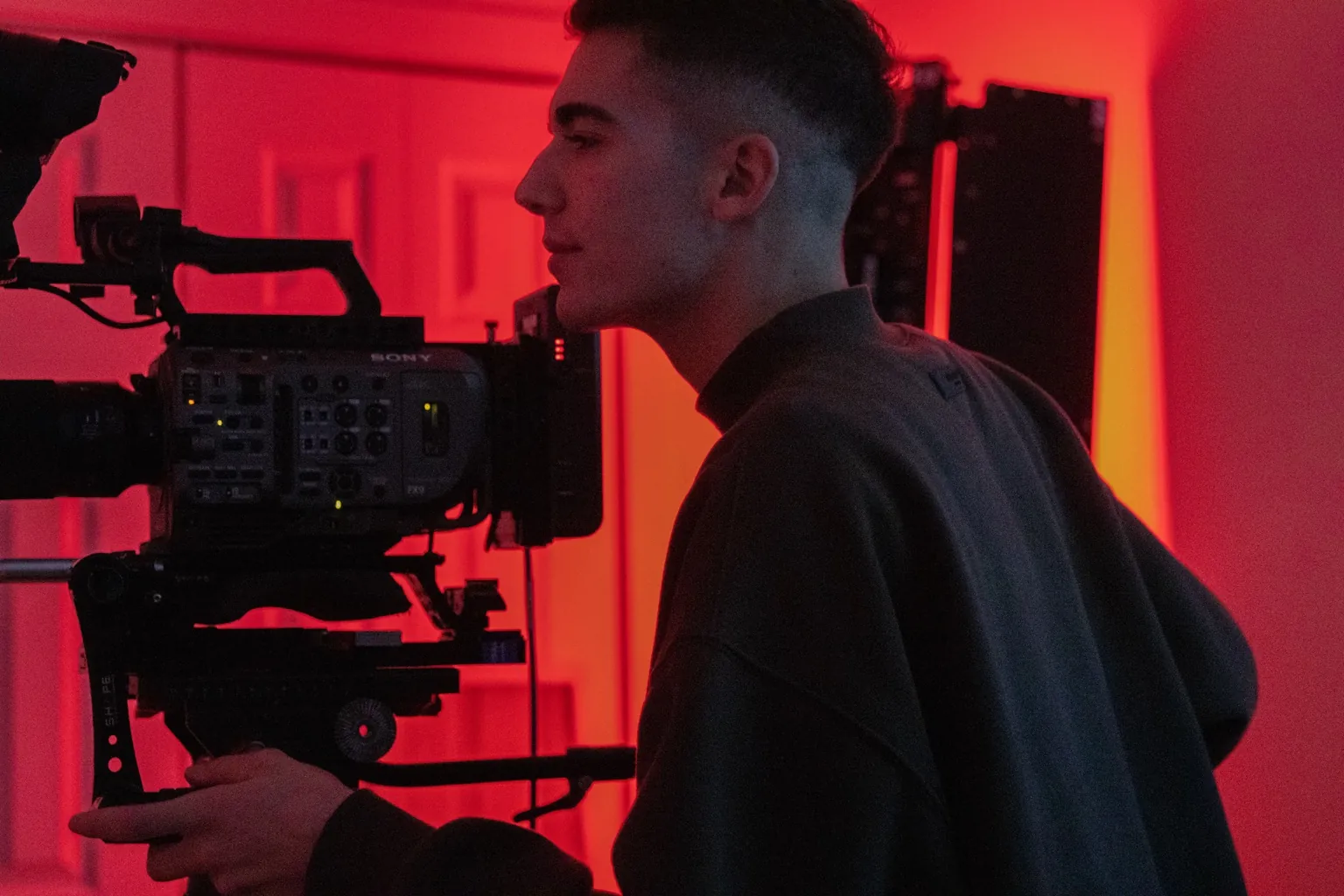 A Production videographer with a cinema camera in a red-lit studio